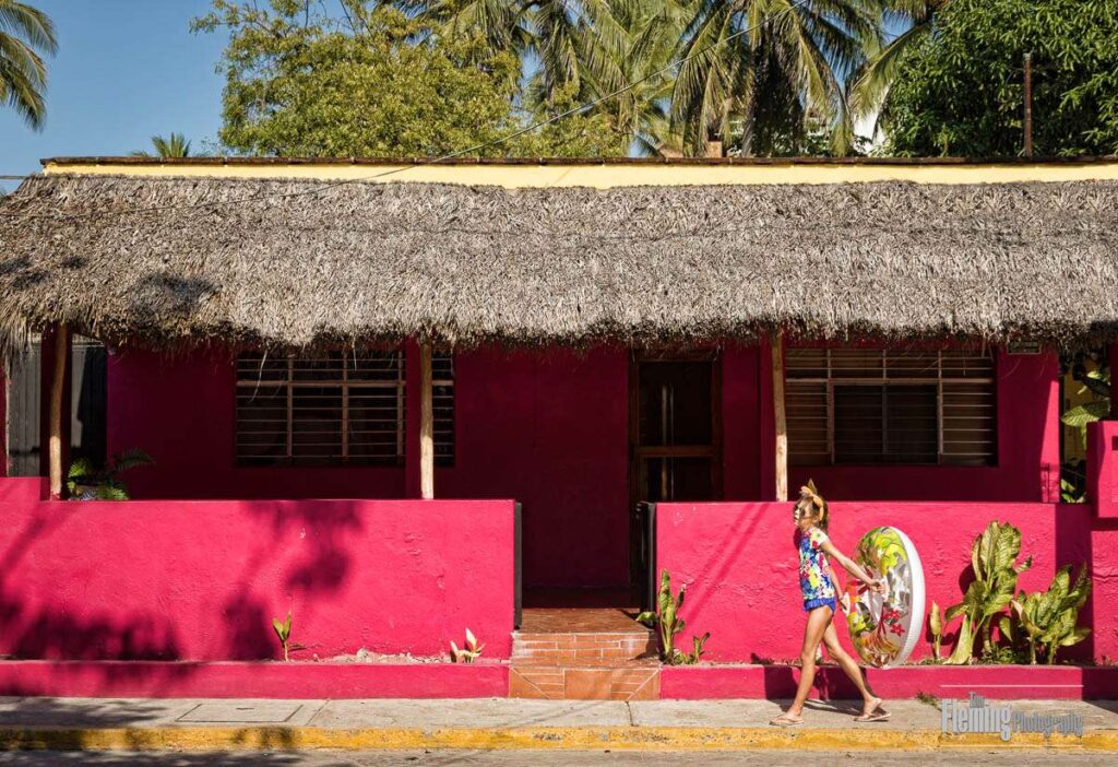Girl walking to the beach carrying an inflatable float toy, colorful pink red house