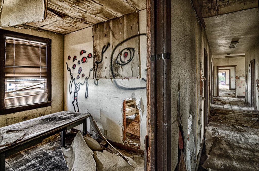 Dilapidated room in abandoned building with graffiti on walls, broken furniture, and peeling paint.