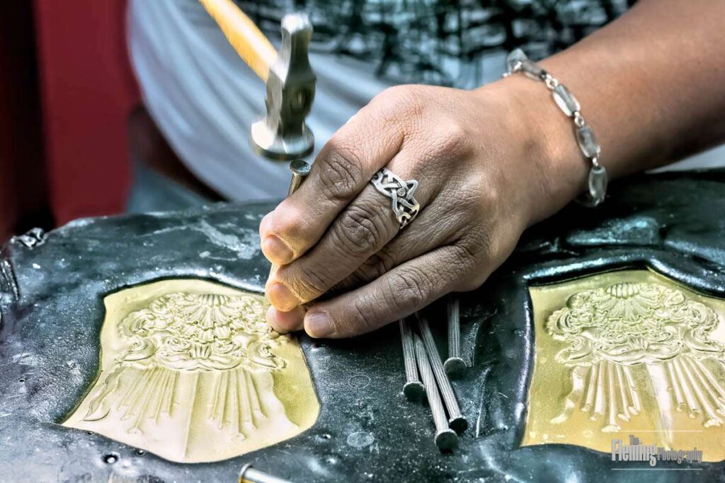 Closeup of metalsmith at work using hammer and nails on copper plate