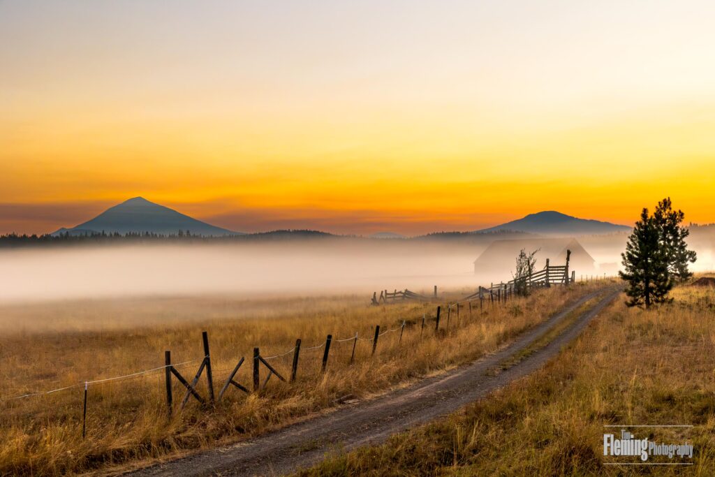 Ground fog at sunrise, dirt road leading to barn, distant mountains, Oregon