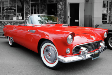 Bright red 1955 Ford Thunderbird convertible against a black and white city street background
