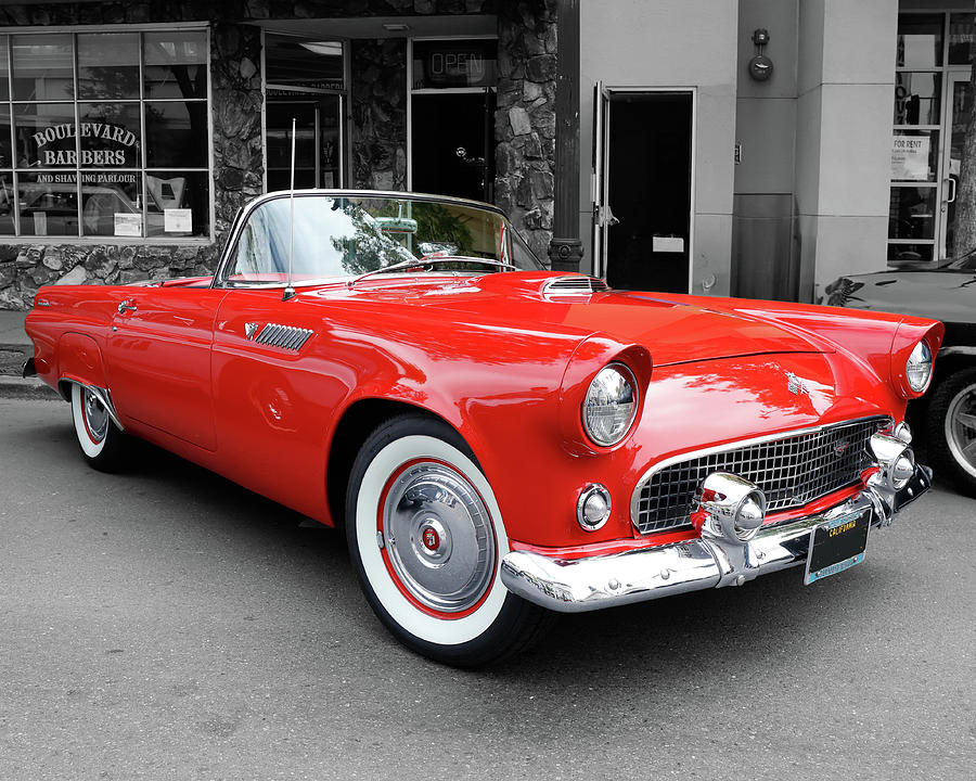 Bright red 1955 Ford Thunderbird convertible against a black and white city street background