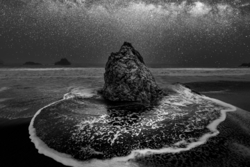 A serene seascape featuring glowing celestial light reflecting off rock formations rising from calm ocean waters under a luminous sky.