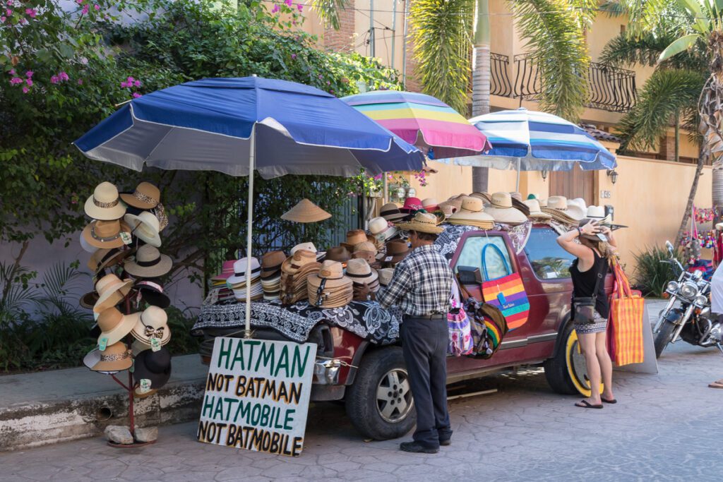 A street vendor selling a large selection of straw hats from the bed of a red pickup truck, shaded by three umbrellas.