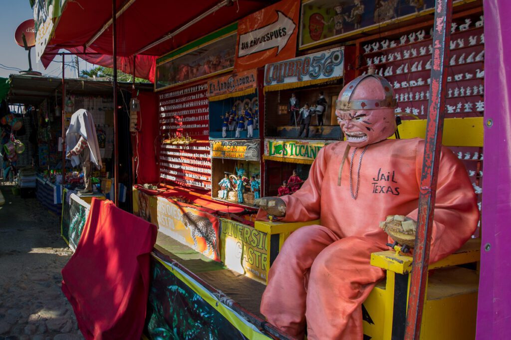 Colorful fairground attraction booth with a quirky jail-themed character in orange suit.