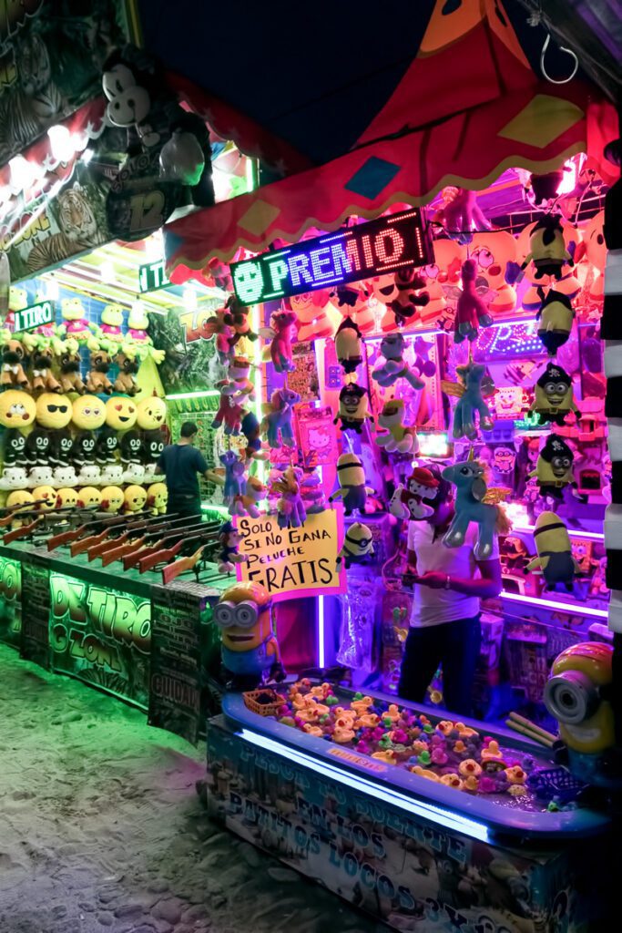 Brightly lit carnival booth with stuffed toys and games at night.