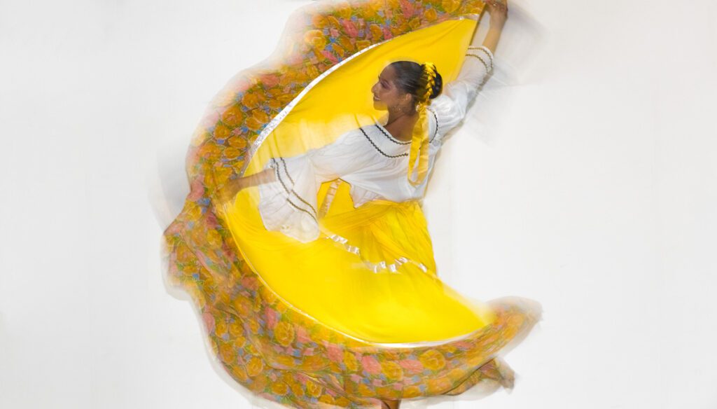 A dancer in a vibrant yellow dress performs a traditional Latin dance.