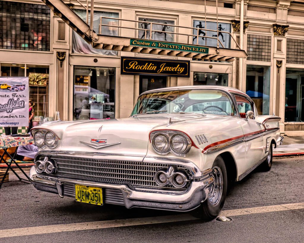 Classic white vintage car parked in front of jewelry store.