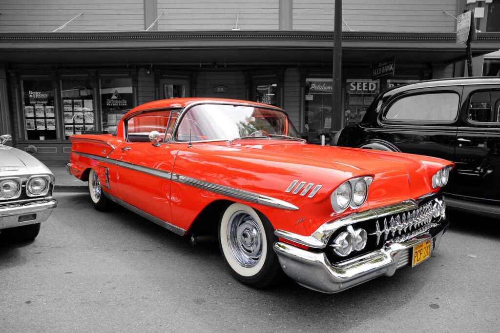 Bright red vintage car parked on a street with two other classic vehicles.