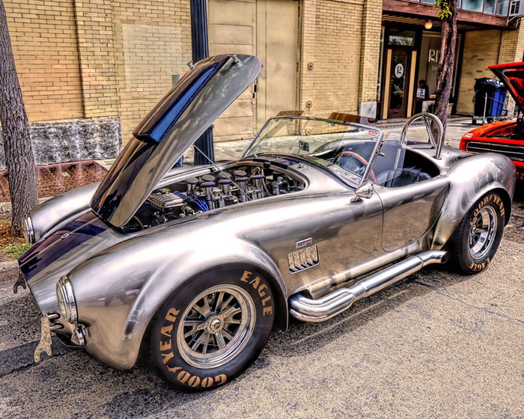 Sleek silver convertible sports car with hood open, showcasing engine, parked on street.