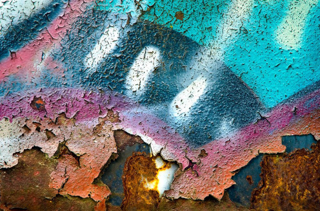 Close-up of colorful peeling paint on rusted metal surface creating abstract texture.