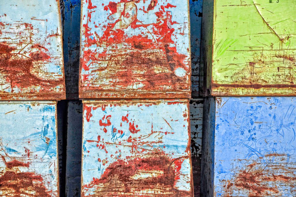 Close-up of rusted metal panels with layers of peeling blue, red, and green paint.