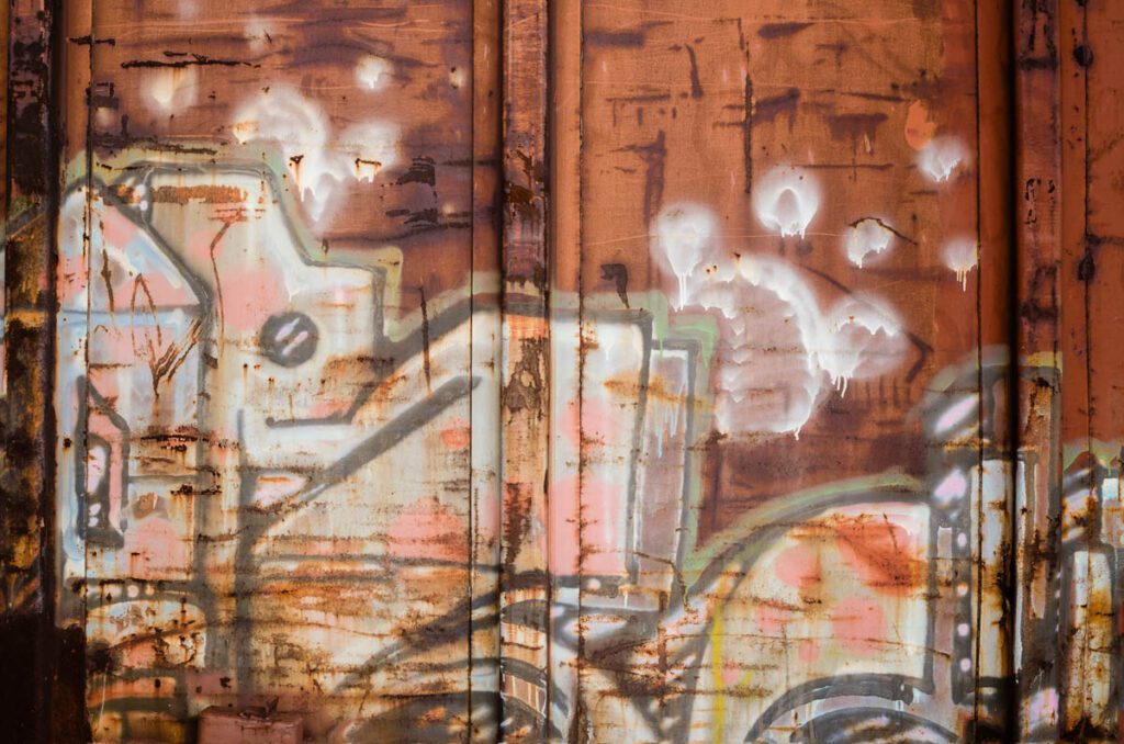 Abstract graffiti on a rusty metal surface with earthy tones and white highlights.
