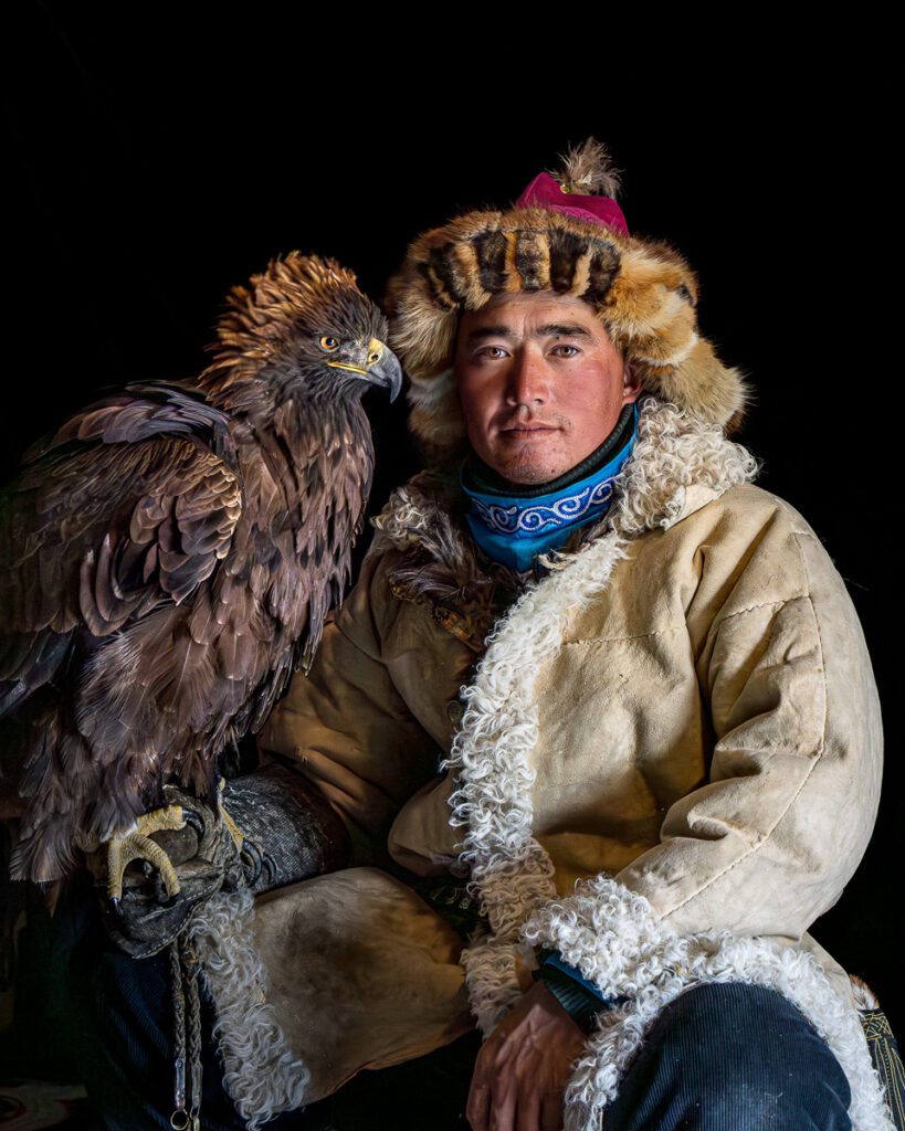 Mongolian eagle hunter with a golden eagle perched on his arm, wearing traditional fur clothing.