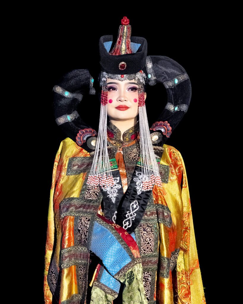 A woman in traditional Mongolian attire with elaborate headpiece and colorful robe.