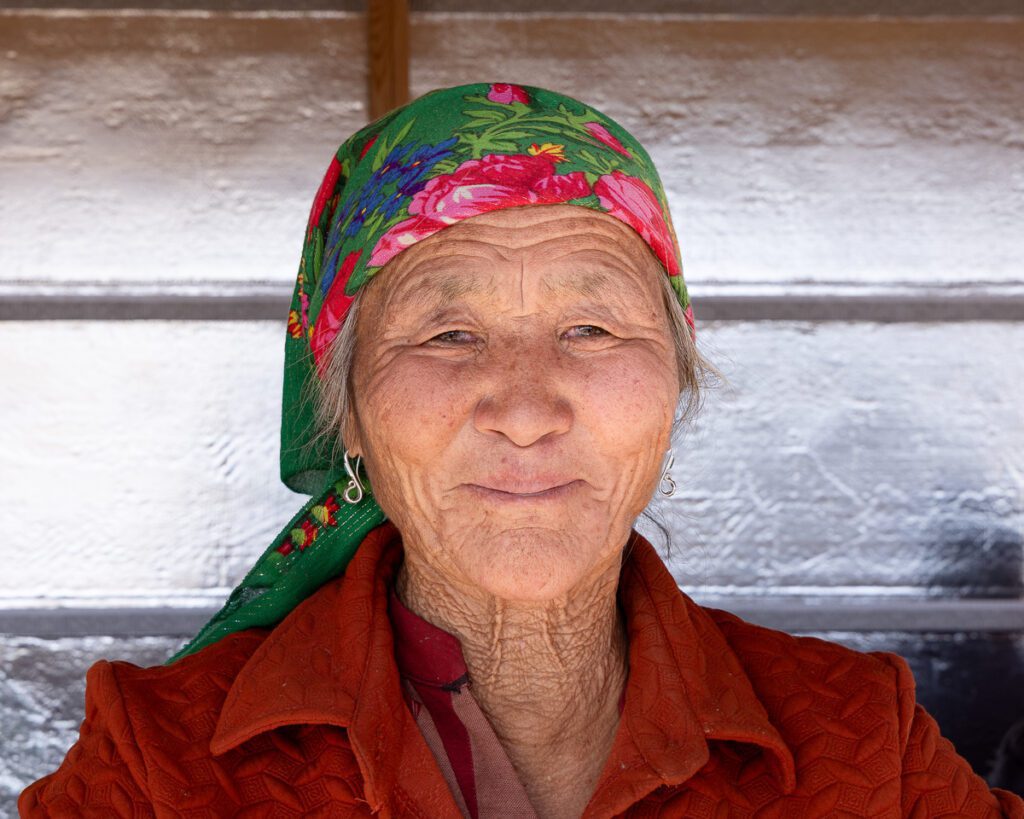 Elderly woman wearing colorful headscarf and red jacket in Mongolia.