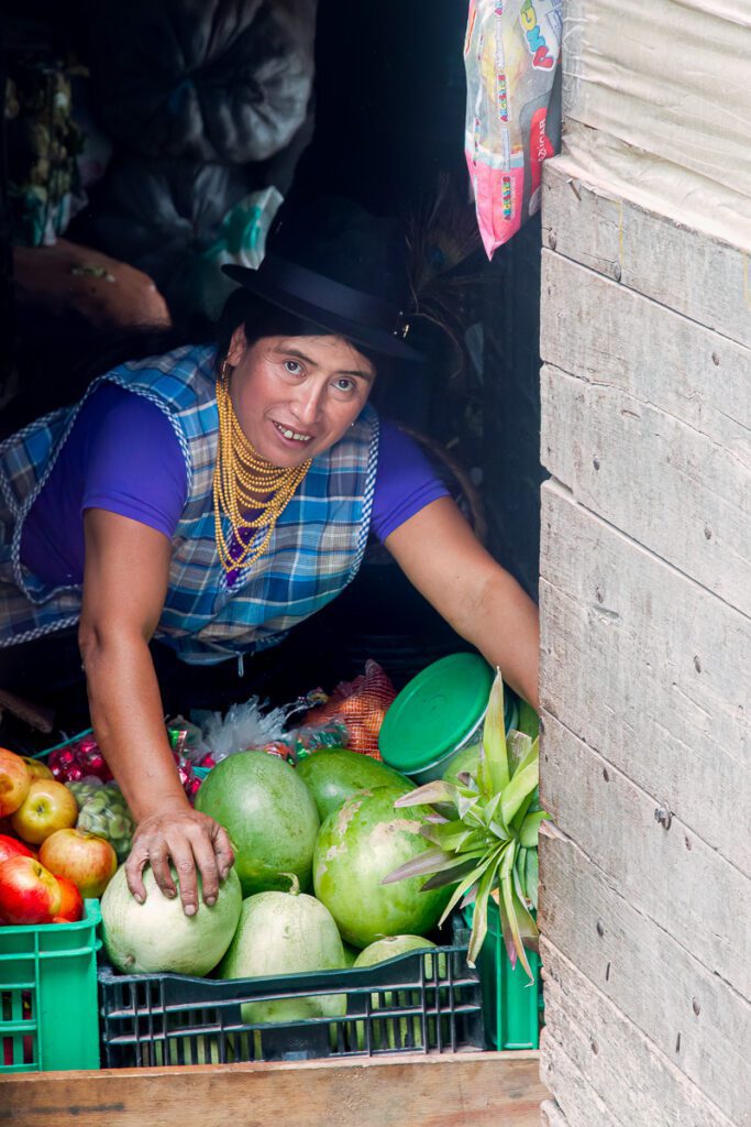A woman in traditional attire arranging fruits in a market stall.