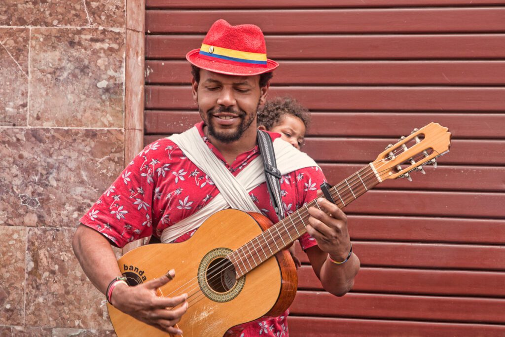 Man in red hat playing guitar with child on his back