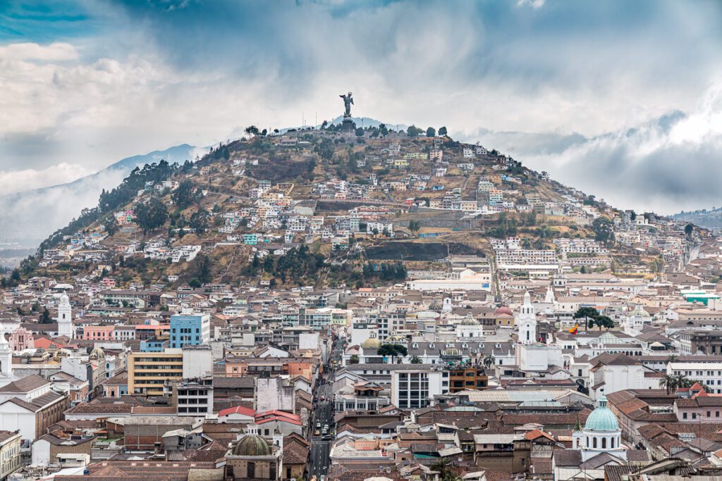 Panoramic view of El Panecillo hill with statue overlooking Quito cityscape.