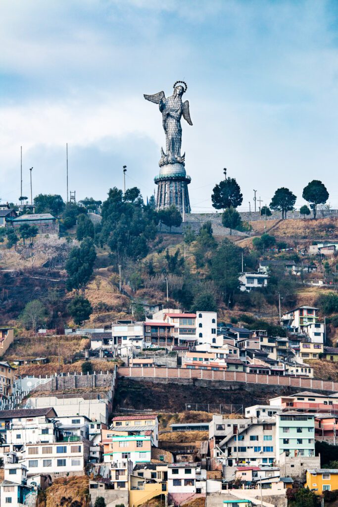 Panoramic view of the Virgen de Quito statue on top of a hill with colorful buildings on the slope.