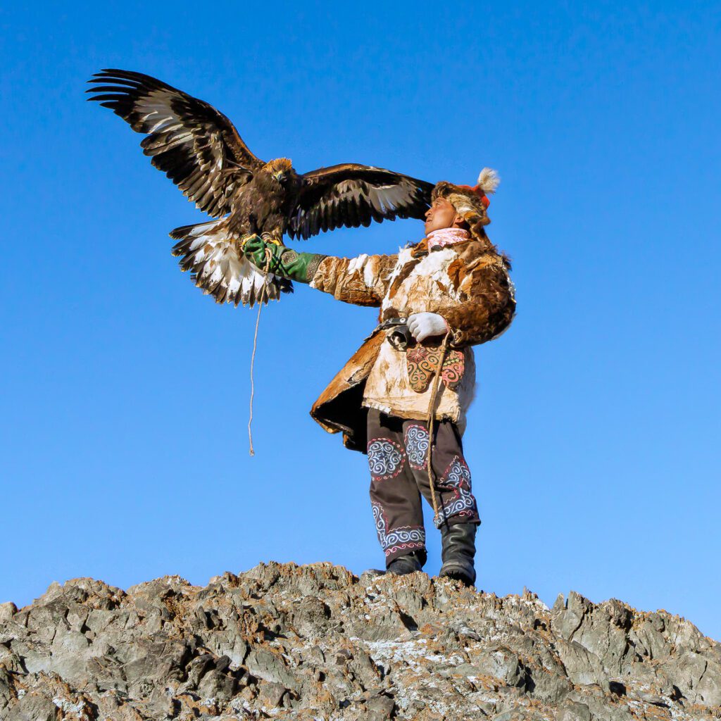 Mongolian eagle hunter in traditional attire with a golden eagle perched on his arm.