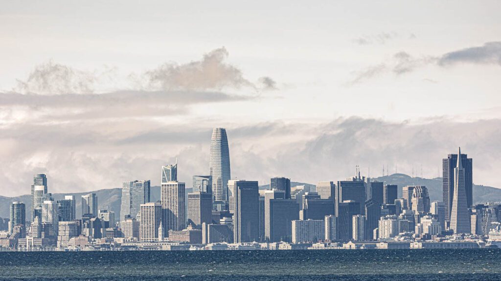 San Francisco skyline with prominent skyscrapers, including the Salesforce Tower, under a cloudy sky.
