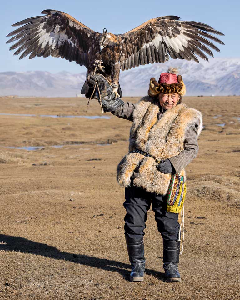 Kazakh eagle hunter holding a golden eagle with wings spread against the Altai Mountains in western Mongolia
