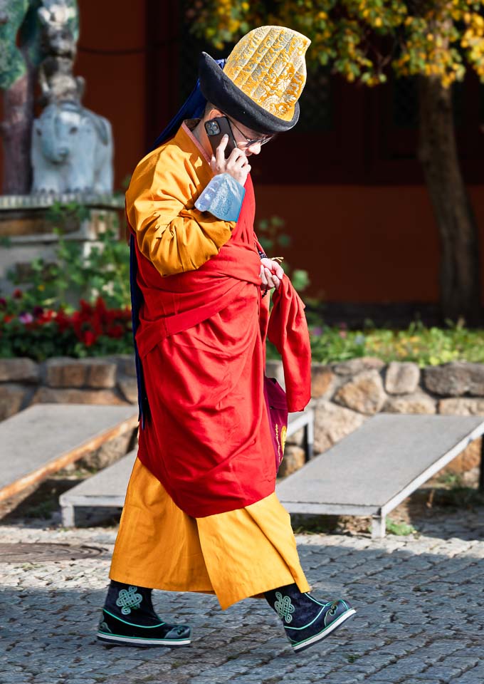 Buddhist monk in saffron and red robes talking on a mobile phone while walking through Gandantegchenling Monastery in Mongolia.