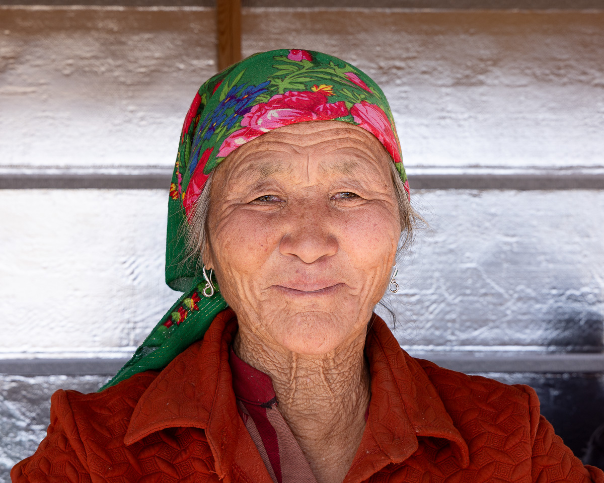 Portrait of an elderly Mongolian woman wearing a colorful floral headscarf and red jacket