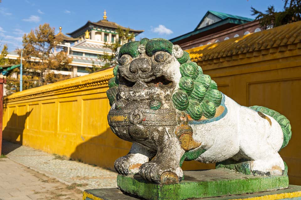 Stone guardian lion beside a yellow monastery wall at Gandantegchenling Monastery in Ulaanbaatar, Mongolia